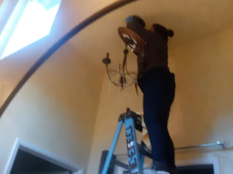 Electrician installing a chandelier in a Olympia Heights residence
